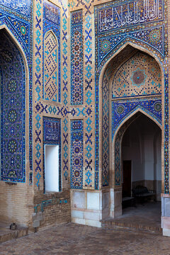 Ornate tiled facade with pointed arches at Shah-i-Zinda necropolis in Samarkand. Intricate blue and turquoise mosaic patterns with Arabic calligraphy adorn the brick walls. Ideal for travel, heritage.