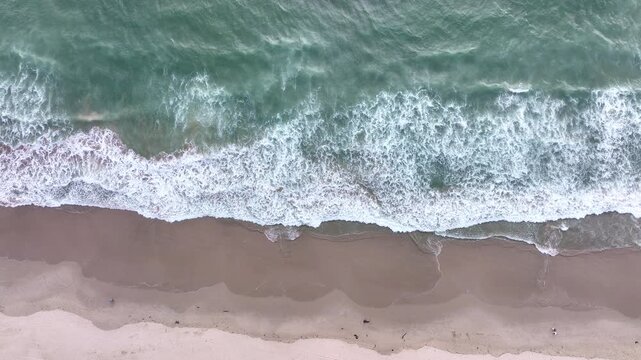 Sea waves rolling to shore. Ocean surf pushing to land. Foamy waves hitting shore. Sea water swirling on coast. Waves breaking on coastline. Rolling ocean waves pattern. Sea foam moving on sand.