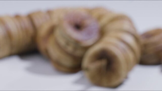 Macro rack focus transition shot shifting focus to reveal a traditional string garland of sweet dried figs, highlighting dry fruit texture, organic snacking, and rich nutrition.