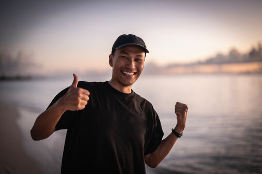 Smiling Asian man celebrates on a beach at sunset