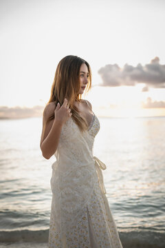 Woman in a lace dress looks out over the ocean at sunset