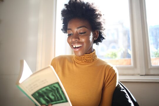 Joyful young woman enjoying a book by the window