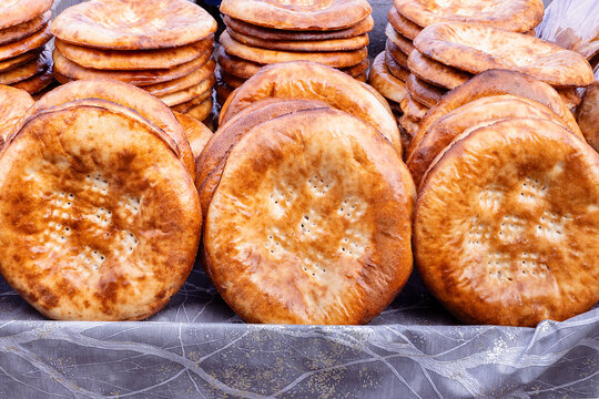 Stacks of traditional Uzbek flatbread displayed at a bazaar in Bukhara. Golden round loaves with decorative patterns are piled for sale, ideal for food culture and travel content.