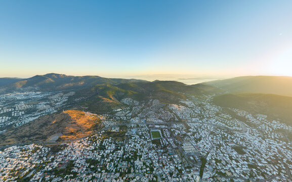 Bodrum, Turkey. High-altitude morning panorama capturing urban white geometry against majestic mountain range with coastal marina in crystal clarity. Aerial view