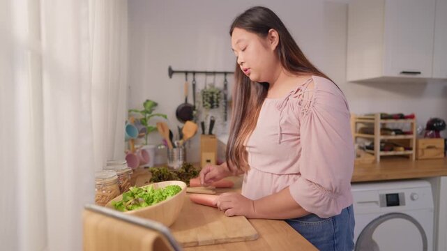 Asian young plus-size woman cooking healthy salad in kitchen at home.