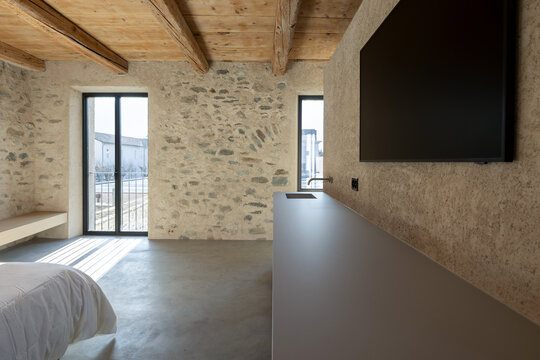 The interior of a bedroom with stone walls, a wooden ceiling and a polished concrete floor.