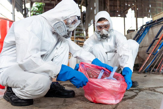 Close-up of professional hazmat workers safely packing contaminated waste into a hazard bag after a chemical spill cleanup in a manufacturing plant, ensuring corporate safety compliance.