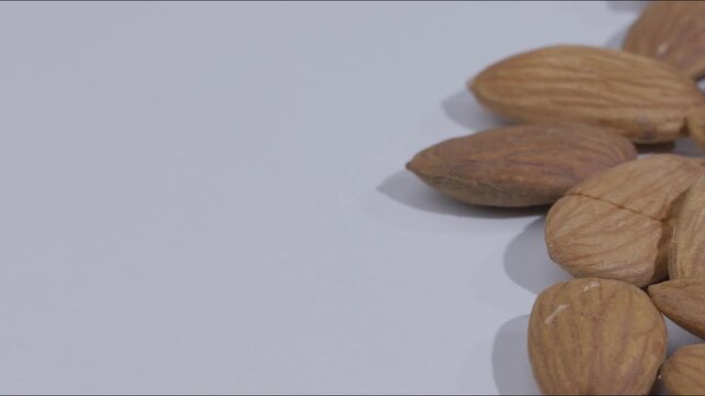 Smooth camera slide transition revealing a pile of fresh crunchy raw almonds on a clean white surface, highlighting dry fruit texture, healthy snacking, and rich organic nutrition.