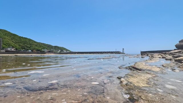 Low Angle Water Surface View Of Clear Coastal Tide Pool Towards Distant Lighthouse, 4K b-roll