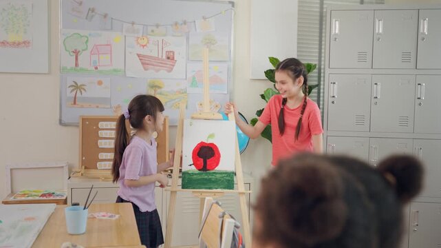 Caucasian girls presenting drawing artwork to classmates in classroom. 