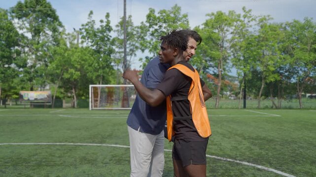 Football coach explaining game strategy to African player during training. 