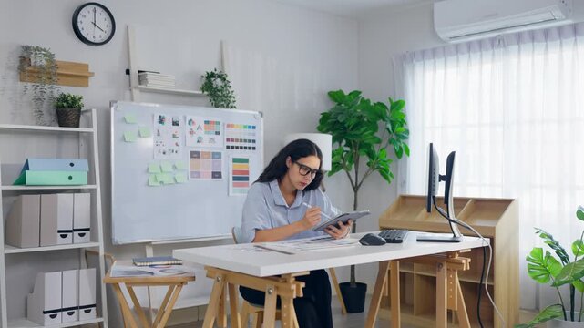 Young Hispanic woman designer sitting at her desk, working in an office. 