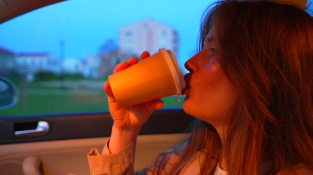 Caffeinated woman enjoys a drink while sitting inside a vehicle at dusk. Static close-up profile and front view shot.