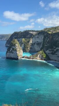 A scenic view of rocky cliffs by a turquoise sea under a clear blue sky. The landscape features lush greenery and gentle waves lapping at the shore.