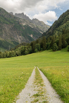 Guttannen, Switzerland. Mountain hiking trail leading through alpine meadow toward rugged peaks in the Bernese Alps