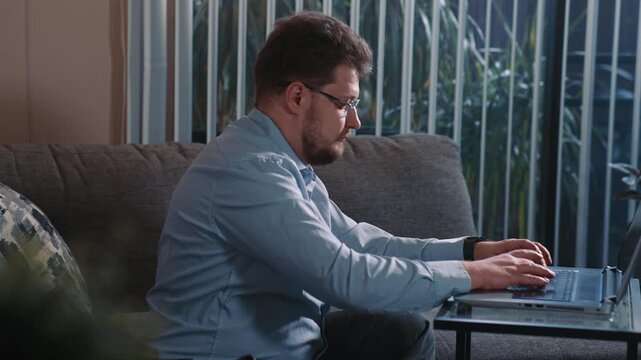 Man typing on laptop working from home near window completing online tasks and remote work on computer in calm home environment