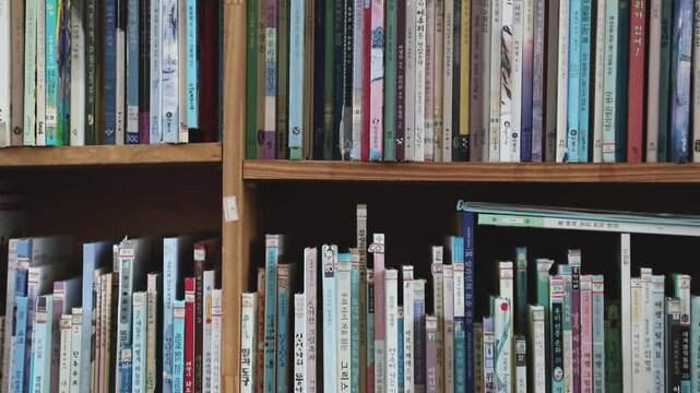 책장에 다양한 종류의 책들이 빼곡하게 꽂혀 있는 실내 모습을 촬영한 장면입니다.