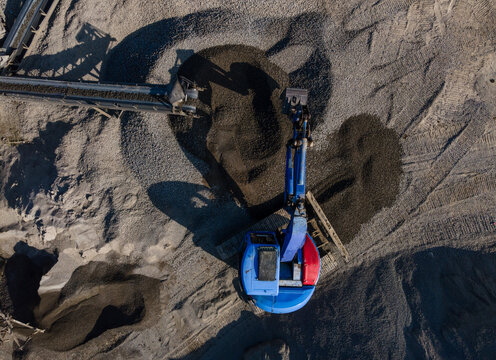 Aerial view of Blue Excavator Working Near Stone Crusher and Stockpiling Area in Industrial Mine Site, Construction and mining site view from above