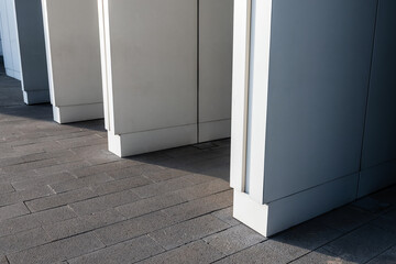 Obraz premium Minimalist modern building exterior with a row of white architectural columns casting long geometric shadows across textured urban pavement, evoking contemporary design and abstraction