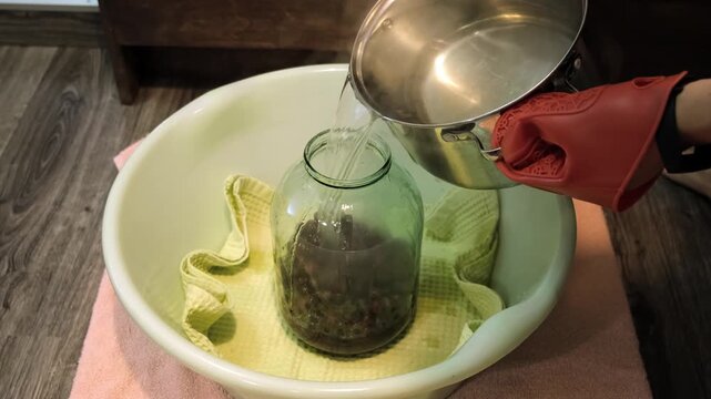 A man canning cherry compote using a manual seaming machine to seal a large glass jar with metal lid. Home canning, food preservation, traditional kitchen, winter storage preparations. A Can Seamer.