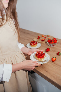 Woman holding homemade strawberry tartlet on kitchen table