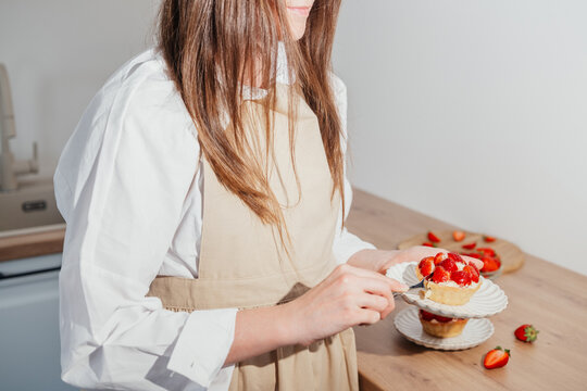 Woman holding homemade strawberry tartlet in bright home kitchen