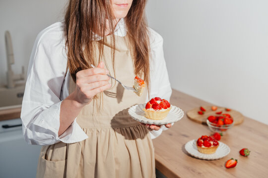 Woman holding strawberry tartlet with cream in kitchen preparation