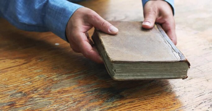 Old antique book with leather cover in man hands, historical aged literature, holy bible or ancient knowledge on grunge wooden table.