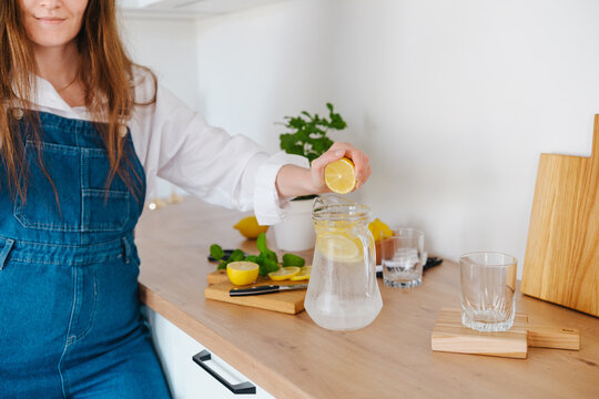 Woman squeezes lemon into pitcher of water with mint.