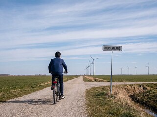 Obraz premium Mann fährt auf Schotterweg an Windrädern vorbei zum Schild Hier entlang