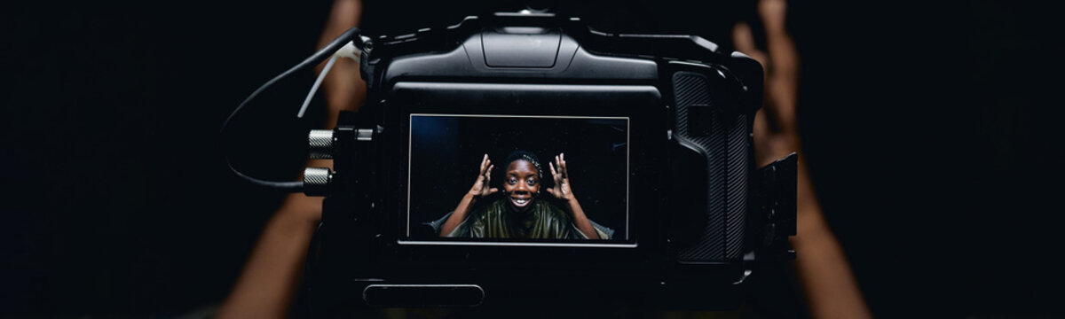 Close up of camera monitor showing Black young adult woman gesturing while recording video content against dark background. Ideal for creator marketing, vlogging, digital media campaigns