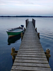 Fototapeta premium A wooden pier extends into a calm lake with a small boat tied to its side.