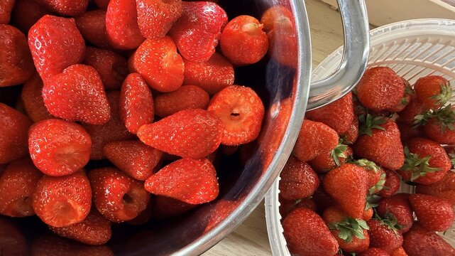 Fresh ripe strawberries in metal bowl and plastic container on rustic wooden table, bright red fruit closeup, summer harvest ingredient for healthy desserts