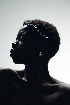 Vertical portrait of young adult Black woman posing in side profile with natural hair and jewelry, expressing beauty identity and confidence. Ideal for skincare, cosmetics, self image marketing