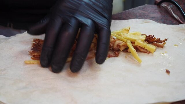 Close up video clip of a person in black gloves adding crispy golden french fries to a layer of cooked, seasoned meat on fresh flatbread, preparing a delicious wrap or sandwich