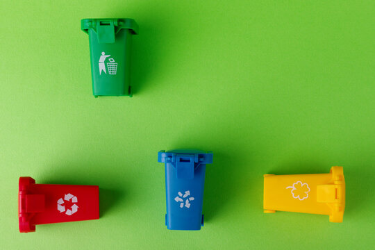 Four recycling bins in red, blue, yellow, and green arranged on a bright green background for environmental themes.