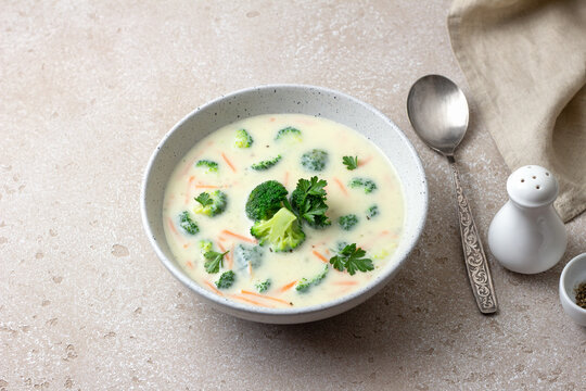 Homemade creamy broccoli soup with potatoes carrots and parsley in ceramic bowl on light textured background