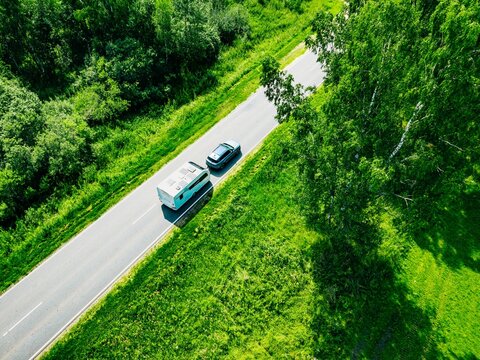 Aerial perspective of a car pulling a caravan roadtripping from a green forest into open fields