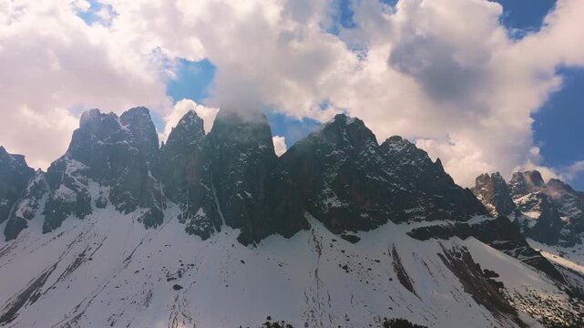 Snow covered Geisler peaks in Puez-Geisler Nature Park, Odle mountain range with clouds. Dolomites aerial