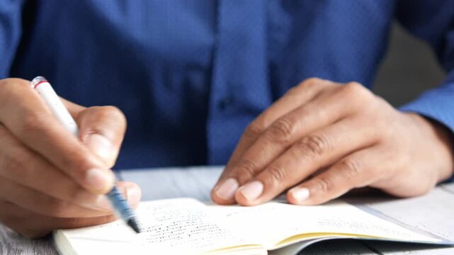 A close-up shot of a person writing in a notebook with a pen, capturing movement and the creative process in detail