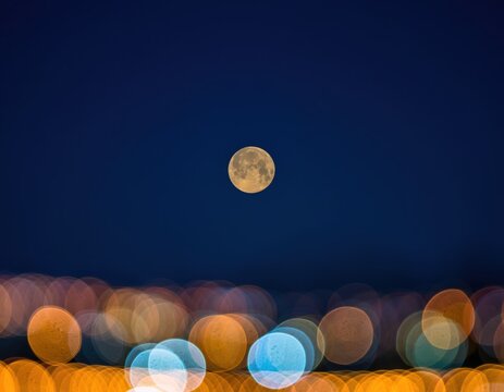 Full moon rising over a blurred city skyline at night with beautiful bokeh lights