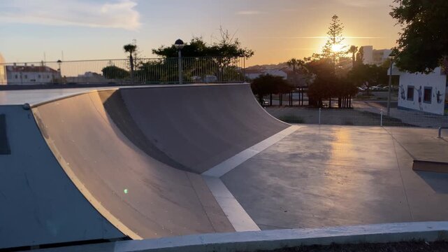 Outdoor skatepark with concrete ramps and ledges reflecting warm golden hour sunlight, creating a peaceful atmosphere