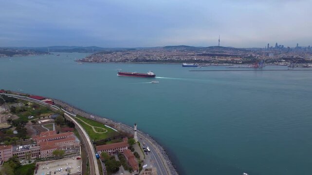 Large tanker navigating Bosphorus Strait, a vital shipping lane, with a small boat following and Istanbul skyline in background. Fantastic aerial view fly reverse drone panorama