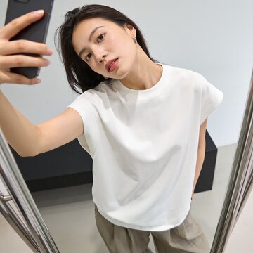 Woman captures a selfie using her smartphone while standing in a bright room, showcasing a minimalist aesthetic and casual lifestyle.