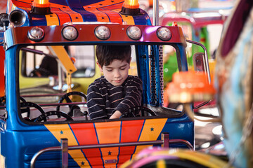 Young boy sitting in colorful blue toy truck on amusement park carousel ride © Oleksii Yemelianov