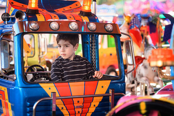 Young boy steering blue toy truck on funfair carousel and looking to the left © Oleksii Yemelianov