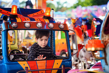 Little boy resting his hand on dashboard of blue toy truck on funfair carousel © Oleksii Yemelianov