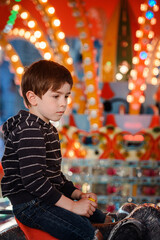 Thoughtful child on fairground carousel with blurred illuminated background © Oleksii Yemelianov