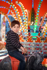A playful young boy sticking his tongue out on an elephant carousel ride at a fairground © Oleksii Yemelianov