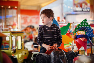 Child holding fairground token and looking away on elephant carousel ride © Oleksii Yemelianov